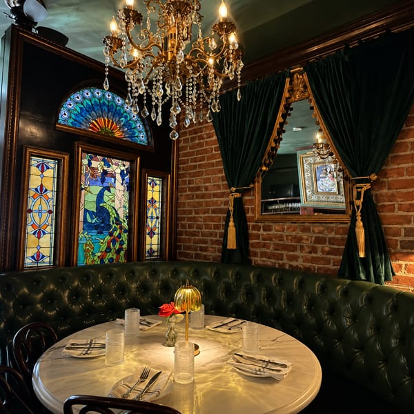 Elegant restaurant interior with a marble table, green leather booth, stained glass, and a chandelier.