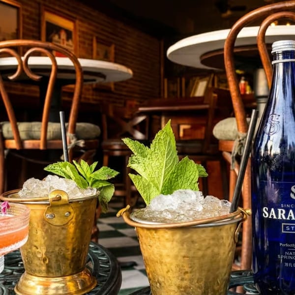 Cocktails, iced mint drinks, and Saratoga water bottles on a table in a cozy restaurant.