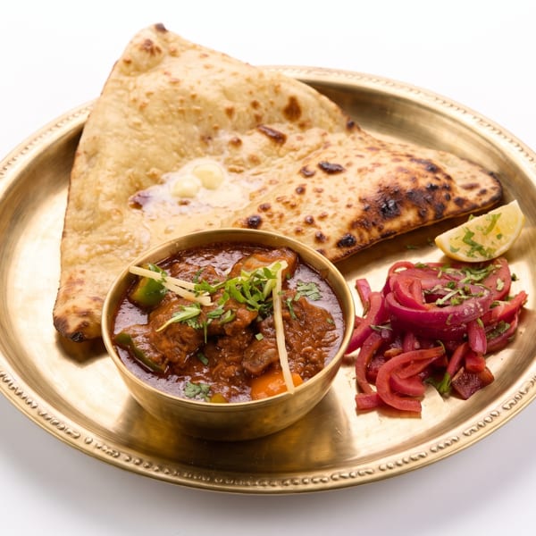 Golden plate with chicken curry, naan bread, pickled red onions, and a lemon wedge.