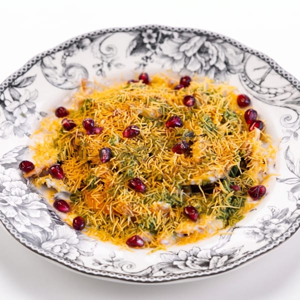 Indian chaat with crispy sev, green chutney, and pomegranate seeds on a decorative floral plate.