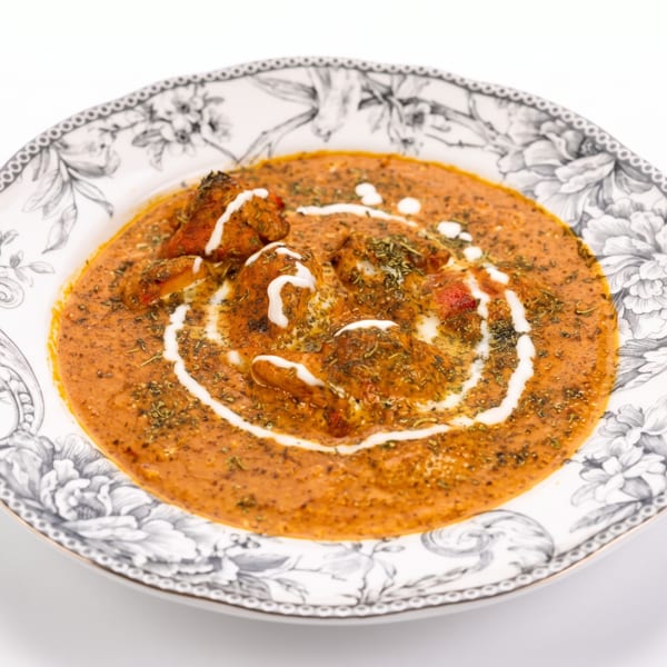 A vibrant orange chicken curry with cream swirls and dried herbs in a decorative plate.